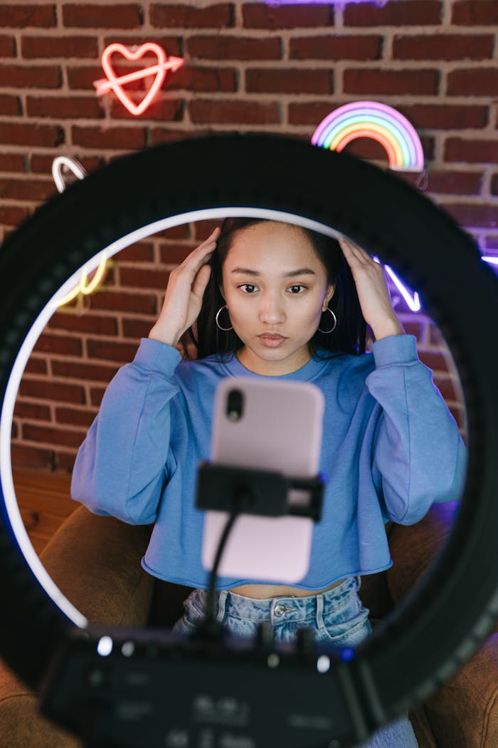 Asian woman recording a video with a smartphone and ring light for streaming purposes.