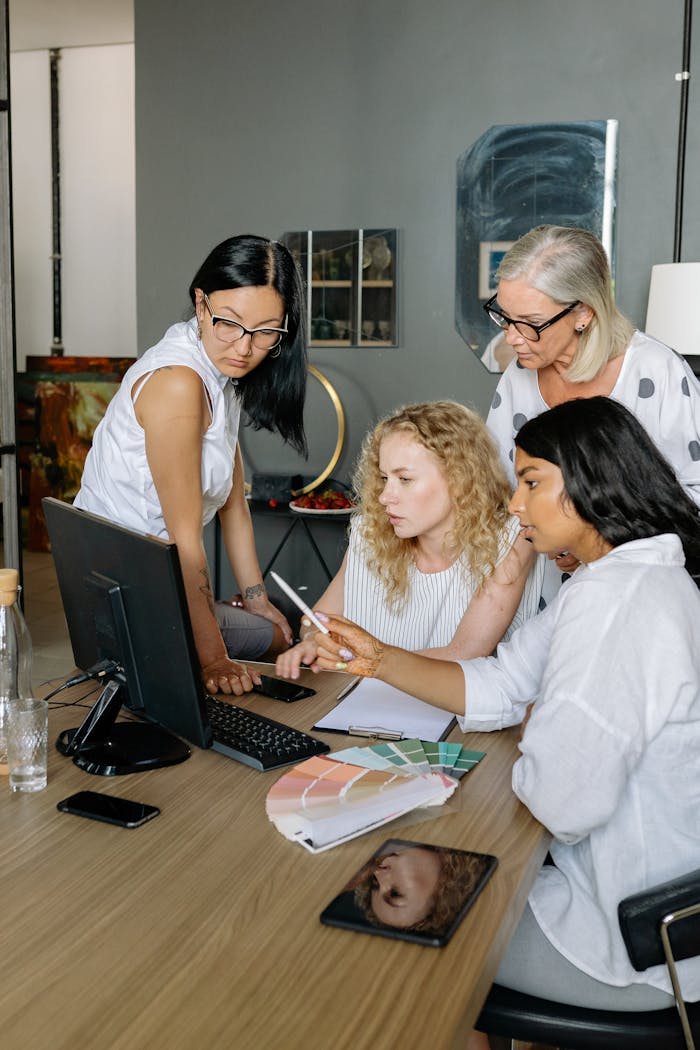 Four businesswomen collaborating over a computer in a modern office, showcasing teamwork and diversity.